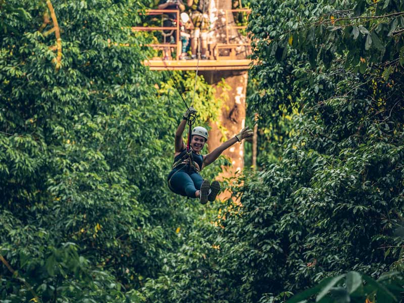 A woman riding a zip line in the middle of a forest.